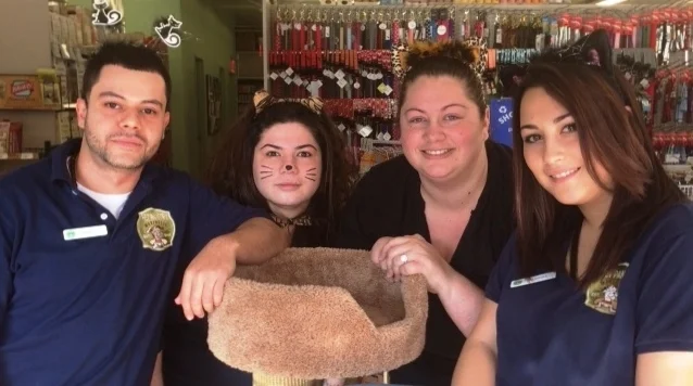 Four Pet Pantry Warehouse staff in navy store polos standing behind a cat tree in the Larchmont store
